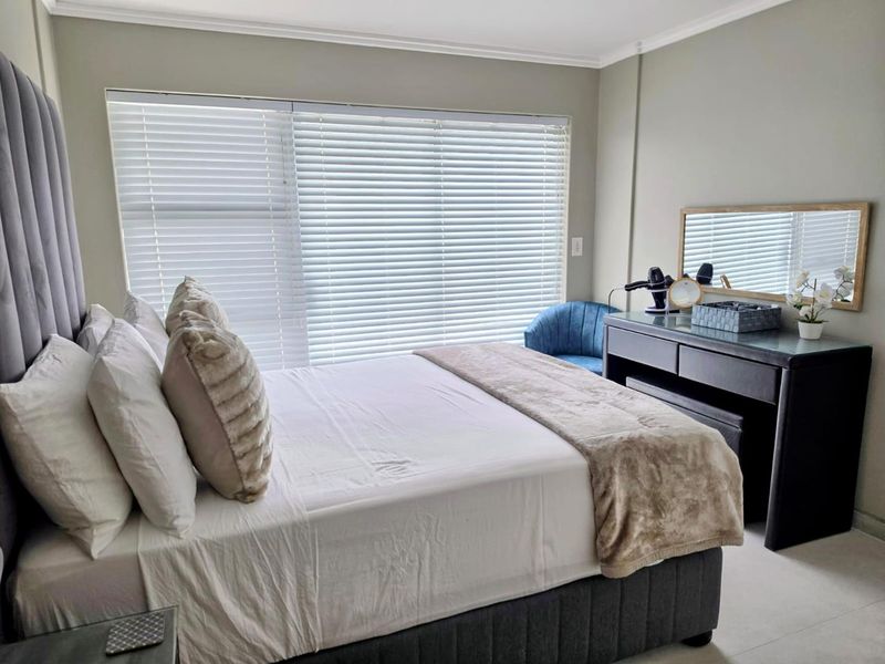 A well-maintained bedroom featuring neutral wall tones, tiled flooring, crown molding, and large windows fitted with venetian blinds.