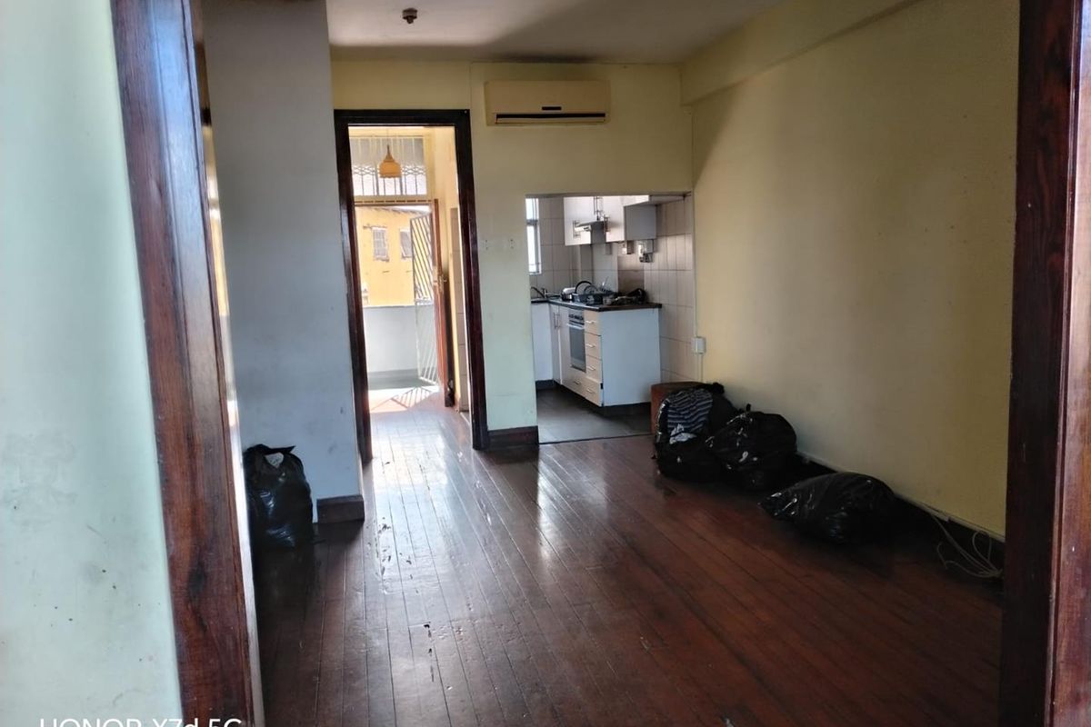 Open plan living area with hardwood flooring and wall-mounted air conditioning, leading to a compact kitchen and balcony access.