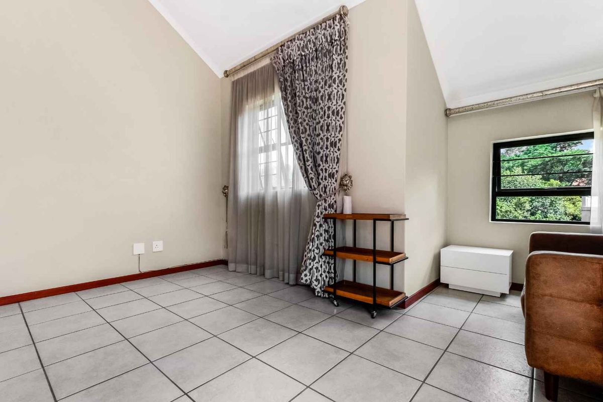 A bright living area featuring high vaulted ceilings, tiled flooring, and large windows that provide natural light and garden views.
