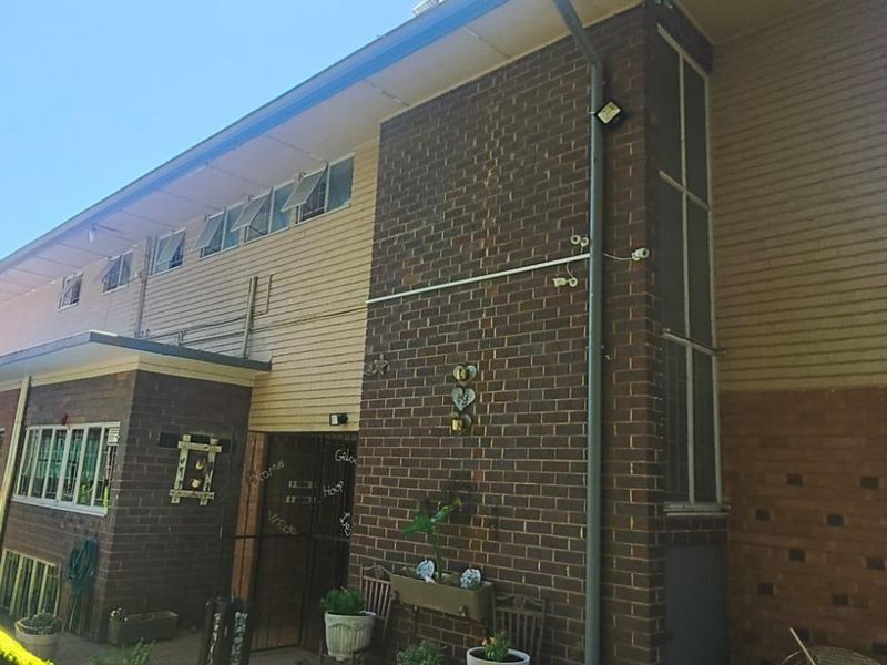 Rear elevation of a two-story house featuring a combination of brick and weatherboard cladding with casement windows and a security gate.