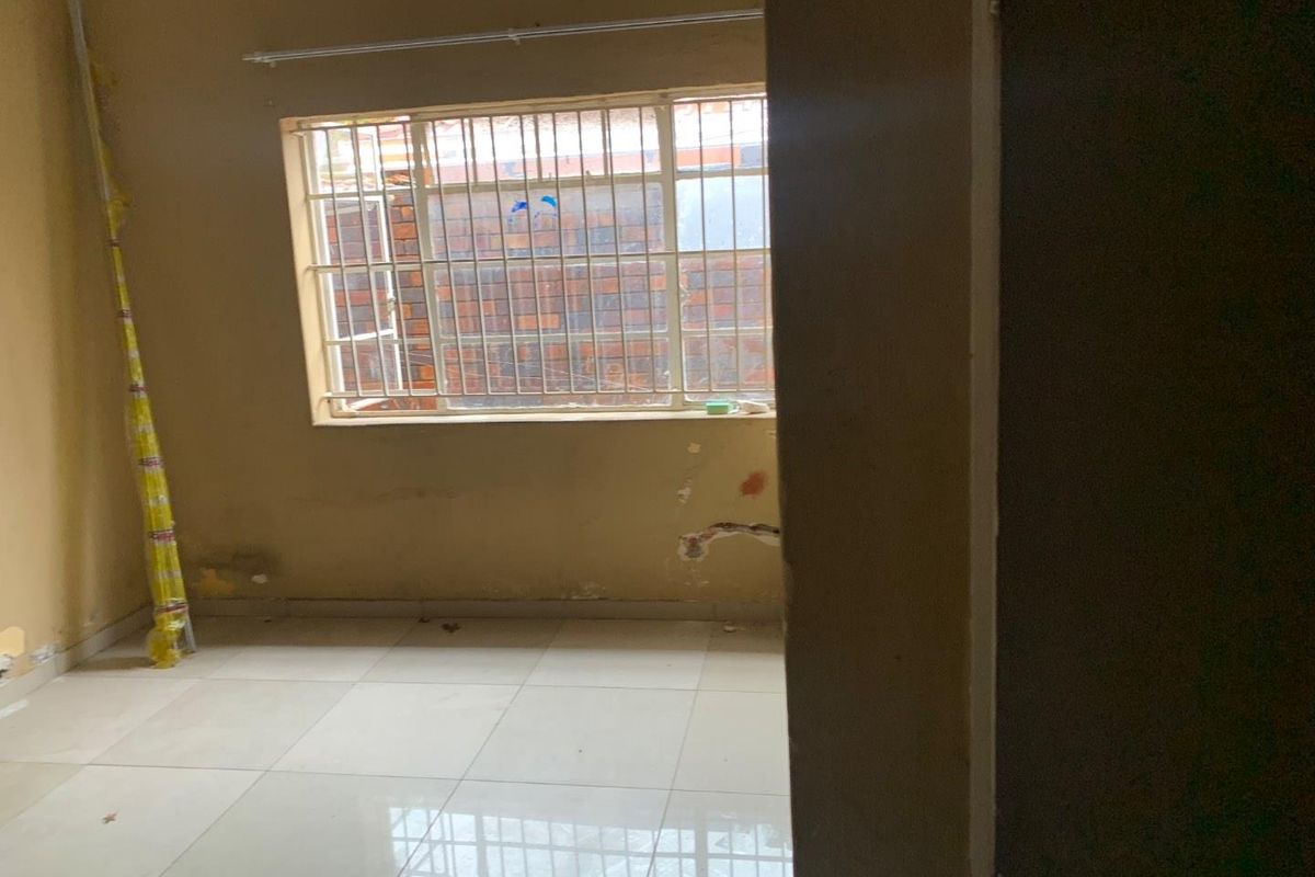 An empty bedroom featuring tiled flooring, a window with security bars, and visible wall damage requiring repair and cosmetic attention.