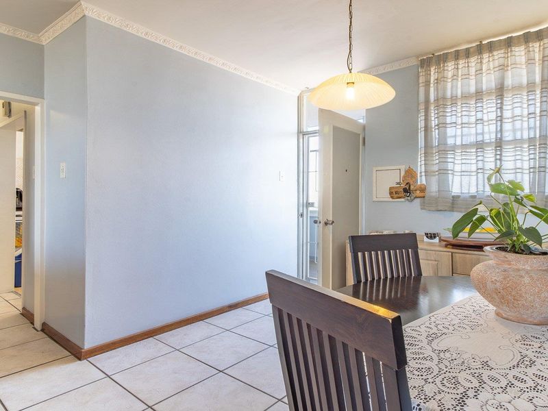 A dining area featuring tiled flooring, decorative ceiling cornicing, and a pendant light fixture, with an adjacent view into a utility or storage space.