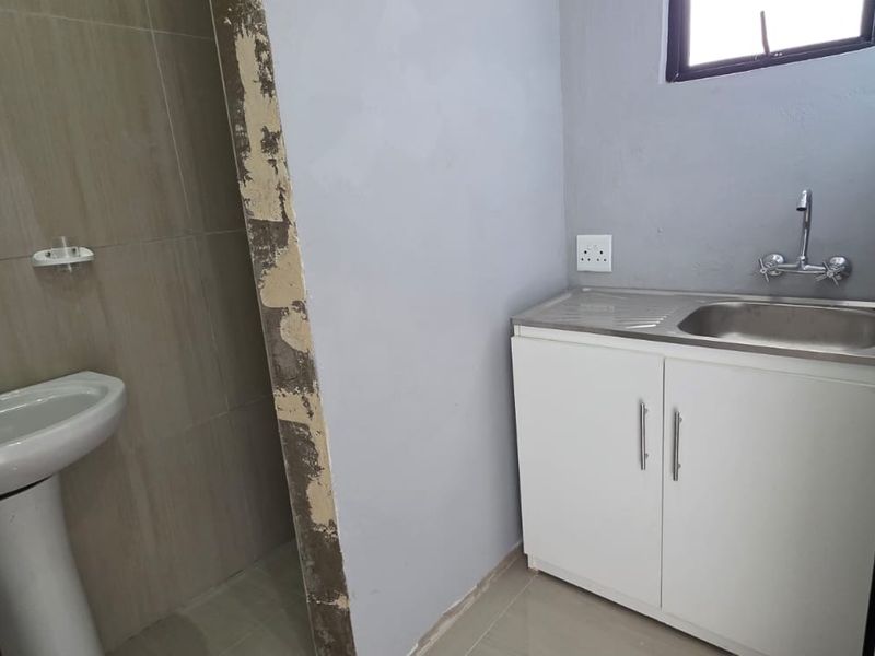 A small bathroom area featuring a pedestal basin and a stainless steel sink with a vanity cabinet, currently requiring finishing touches to the walls.
