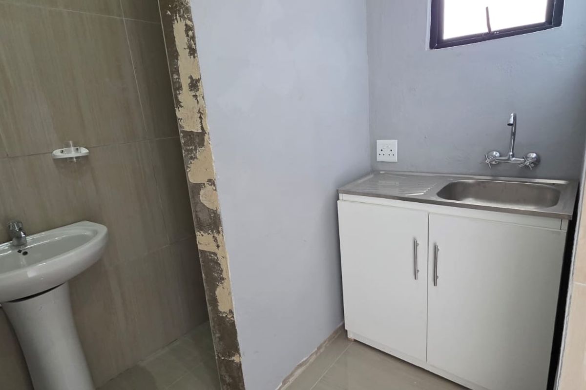 A small bathroom area featuring a pedestal basin and a stainless steel sink with a vanity cabinet, currently requiring finishing touches to the walls.