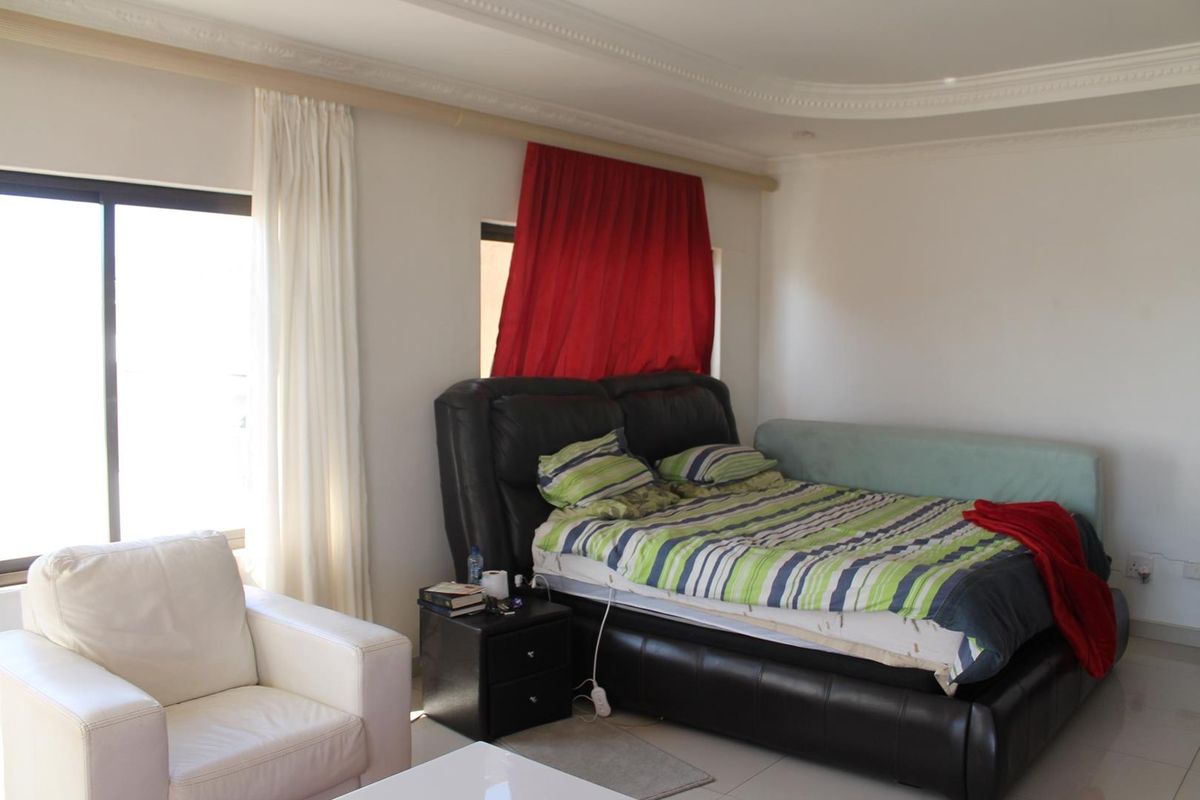 A spacious bedroom featuring tiled flooring, decorative ceiling cornicing, and large windows that provide ample natural light.