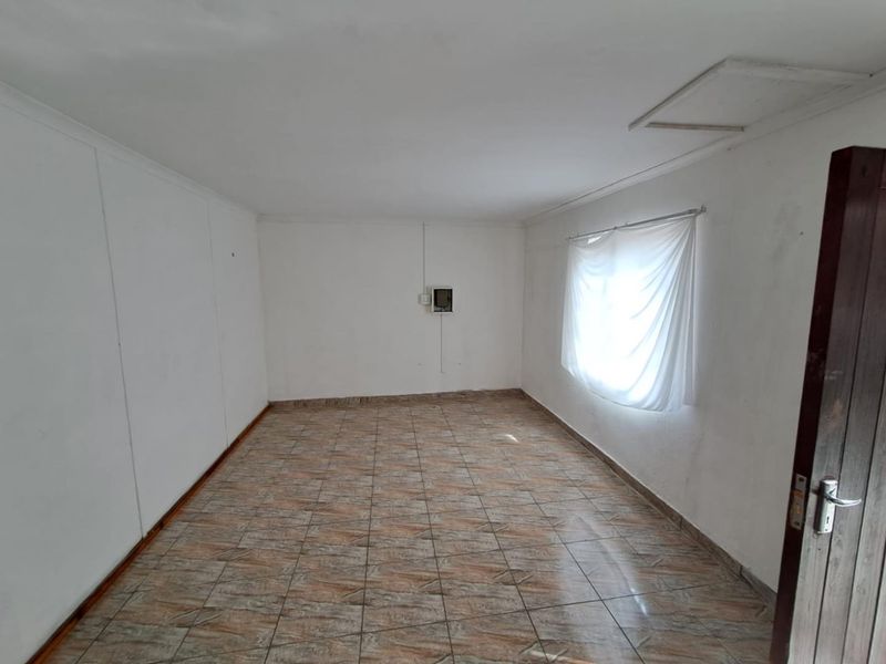 An empty bedroom featuring tiled flooring, a ceiling access hatch, and a wall-mounted electrical distribution board.
