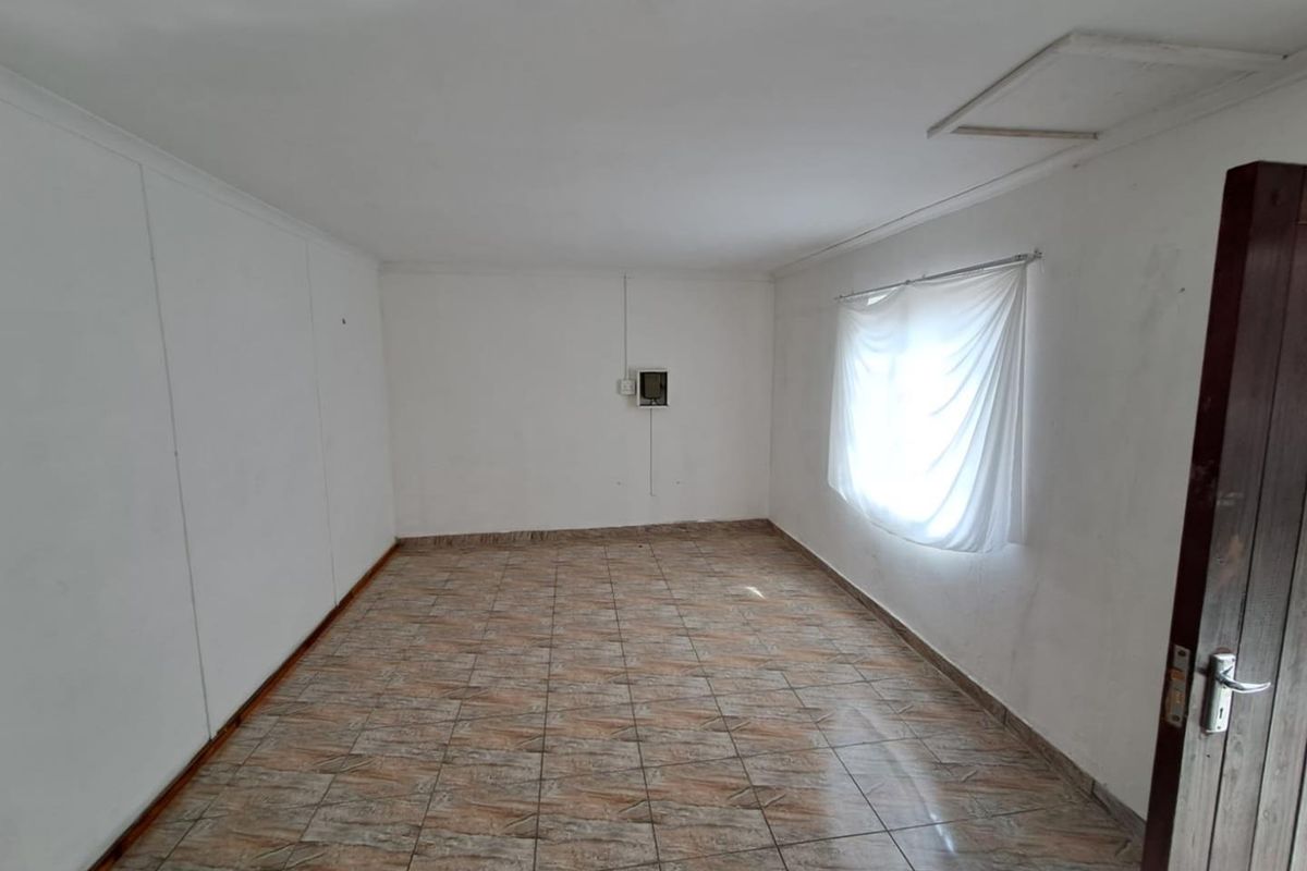 An empty bedroom featuring tiled flooring, a ceiling access hatch, and a wall-mounted electrical distribution board.