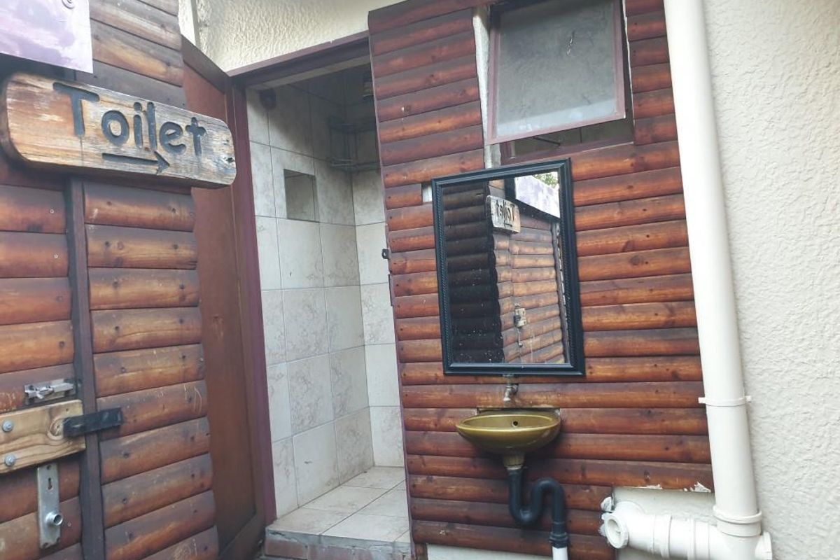 Outdoor bathroom facility featuring a small basin, wall-mounted mirror, and tiled shower area with timber-clad exterior walls.