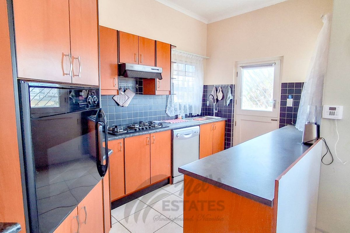 A functional kitchen featuring wood-finish cabinetry, a built-in oven, gas hob, extractor fan, and a breakfast bar with tiled flooring.