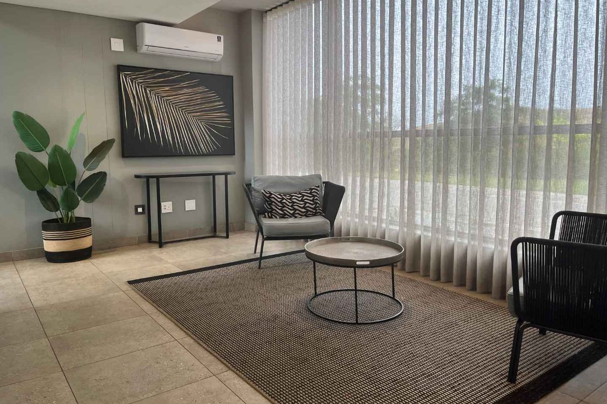 A modern, well-maintained living area featuring tiled flooring, a wall-mounted air conditioning unit, and expansive floor-to-ceiling sheer curtains.