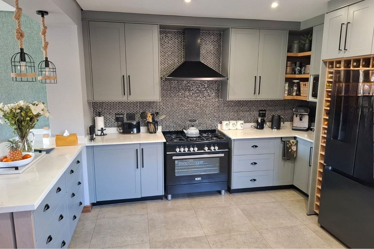 Modern kitchen featuring grey cabinetry, quartz countertops, a mosaic tile backsplash, and a professional-style gas stove with an extractor fan.