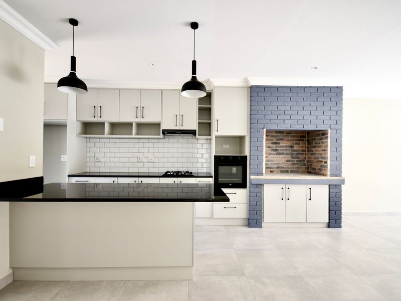 Modern kitchen featuring sleek cabinetry, black granite countertops, subway tile backsplash, built-in oven, gas hob, and a distinctive built-in indoor braai area.