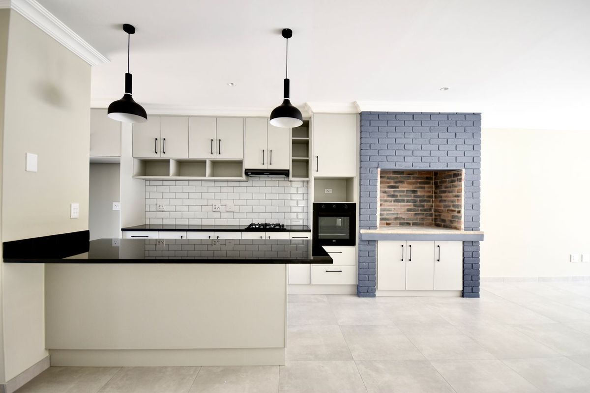 Modern kitchen featuring sleek cabinetry, black granite countertops, subway tile backsplash, built-in oven, gas hob, and a distinctive built-in indoor braai area.