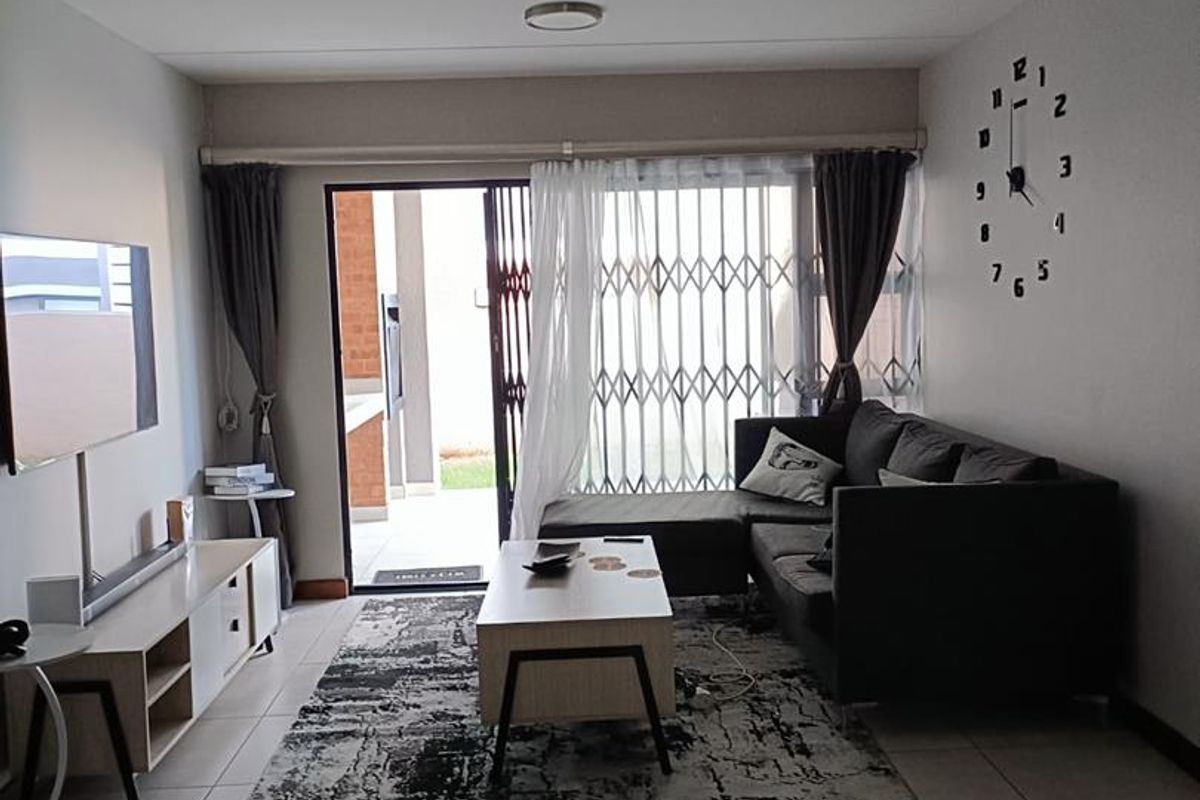 A well-lit living room featuring large format floor tiles, recessed ceiling lighting, and a sliding glass door leading to an outdoor patio area.