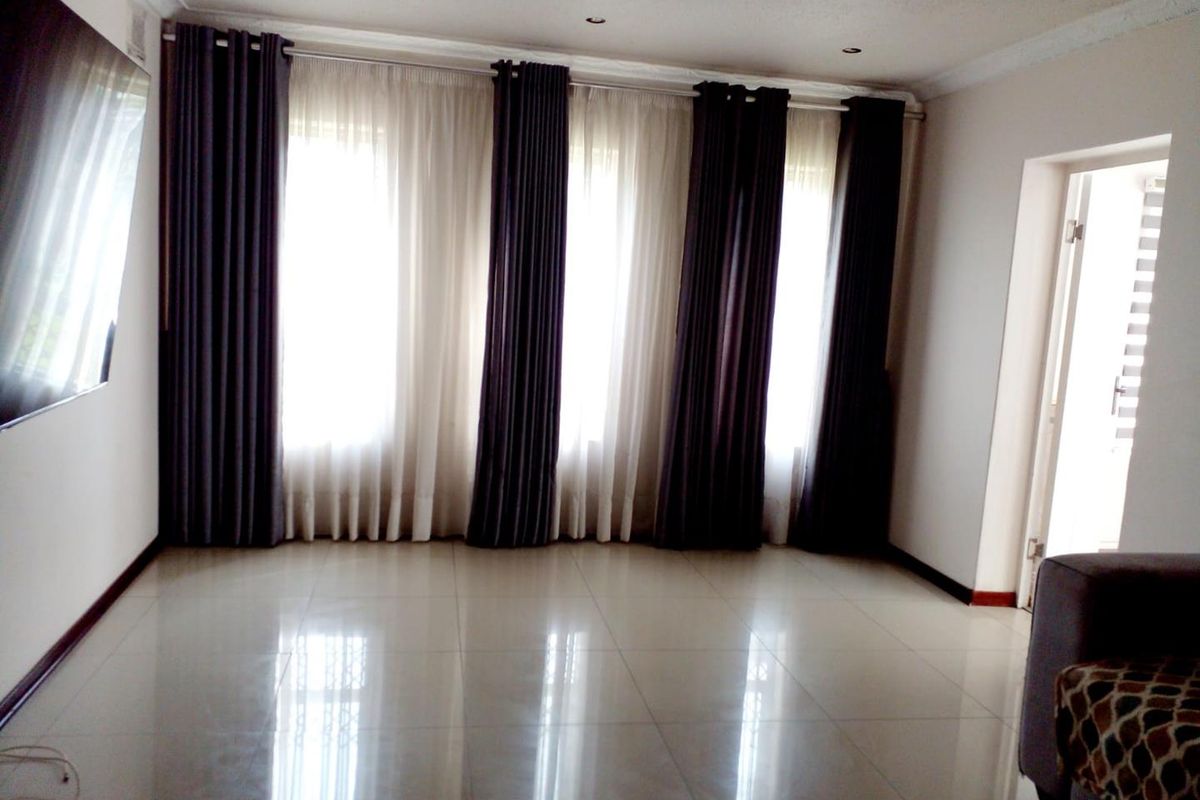 A spacious, empty living room featuring polished tiled flooring, recessed downlighting, and large windows dressed with floor-to-ceiling curtains.