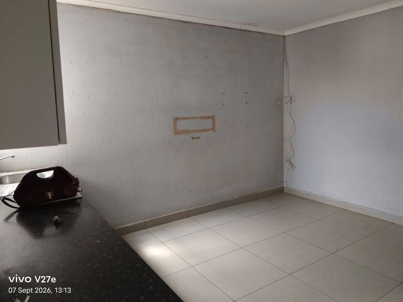 A compact kitchen area featuring tiled flooring and a granite countertop, currently requiring cosmetic updates and finishing to the wall surfaces.