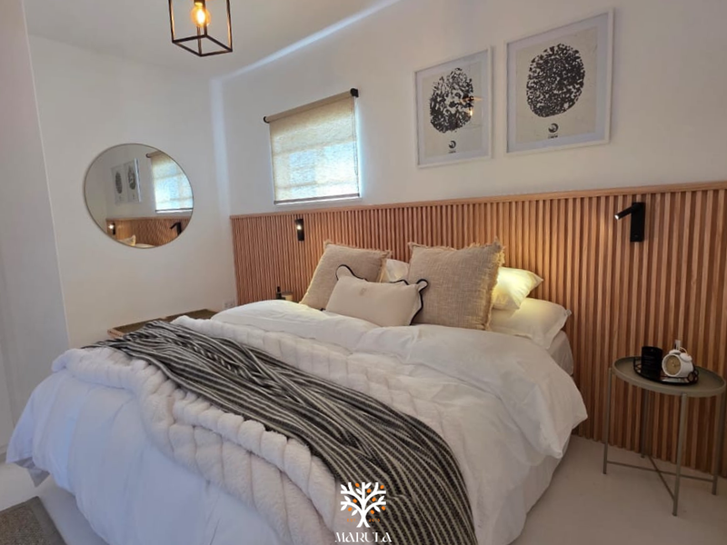 A modern bedroom featuring a stylish timber slat feature wall, integrated wall-mounted reading lights, and neutral finishes.