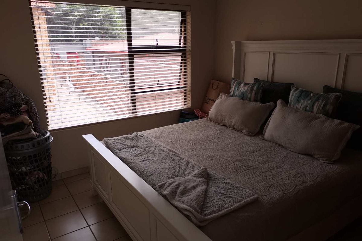 A bedroom featuring tiled flooring and a large window with fitted blinds, providing natural light and a view of the exterior.