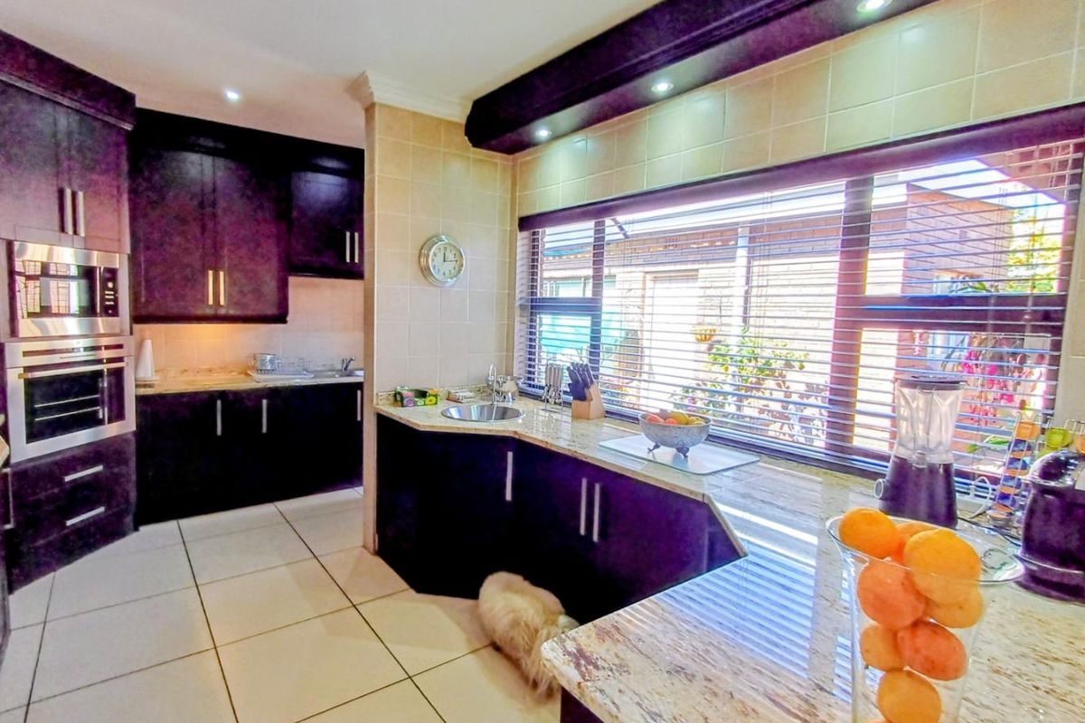 Modern kitchen featuring dark cabinetry, granite countertops, built-in oven and microwave, tiled flooring, and a large window providing ample natural light.
