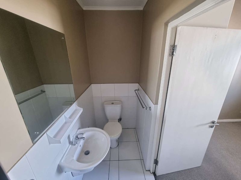 A functional bathroom featuring a pedestal basin, toilet, wall-mounted mirror, and tiled finishes.