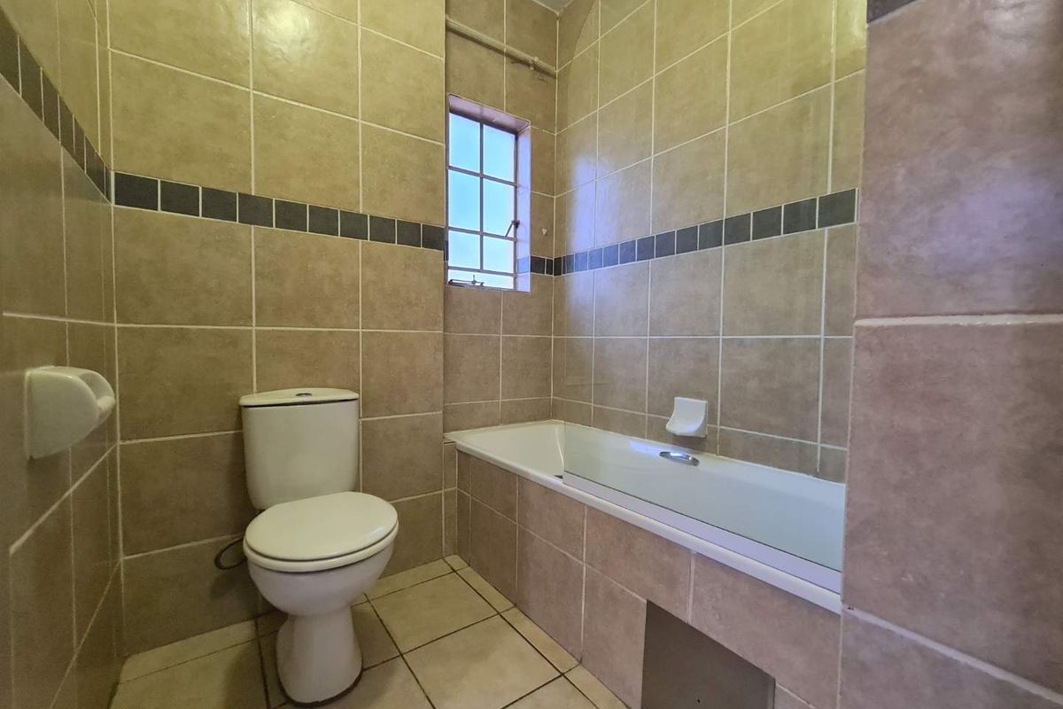 A functional bathroom featuring full-height wall tiling, a standard bathtub, and a toilet, with a small window providing natural light.