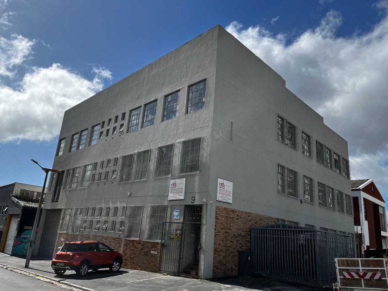 A multi-story industrial building featuring a combination of brick and rendered facade, equipped with security grilles and industrial-style windows.