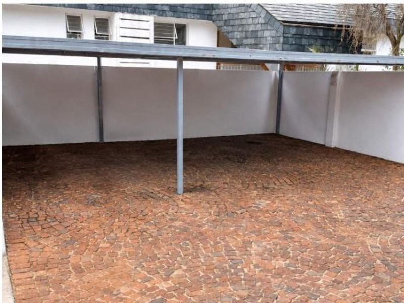 A covered carport area featuring durable cobblestone paving and secure perimeter boundary walls, providing sheltered off-street parking.