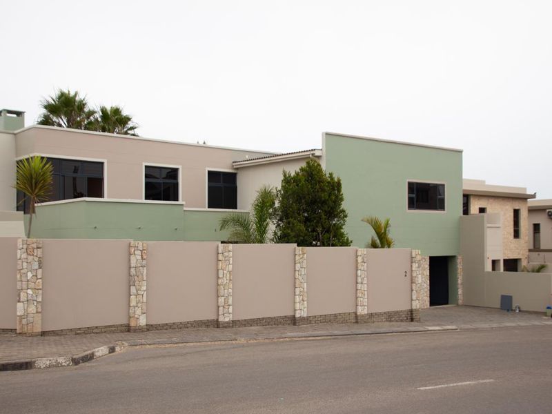 Modern residential property facade featuring a stone-clad boundary wall, paved driveway, and contemporary architectural design with neutral and green exterior finishes.