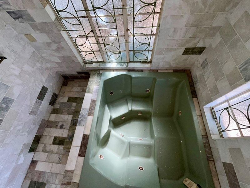 A bathroom featuring a built-in spa bath with tiled surround and flooring, complemented by decorative metal security grilles on the windows.