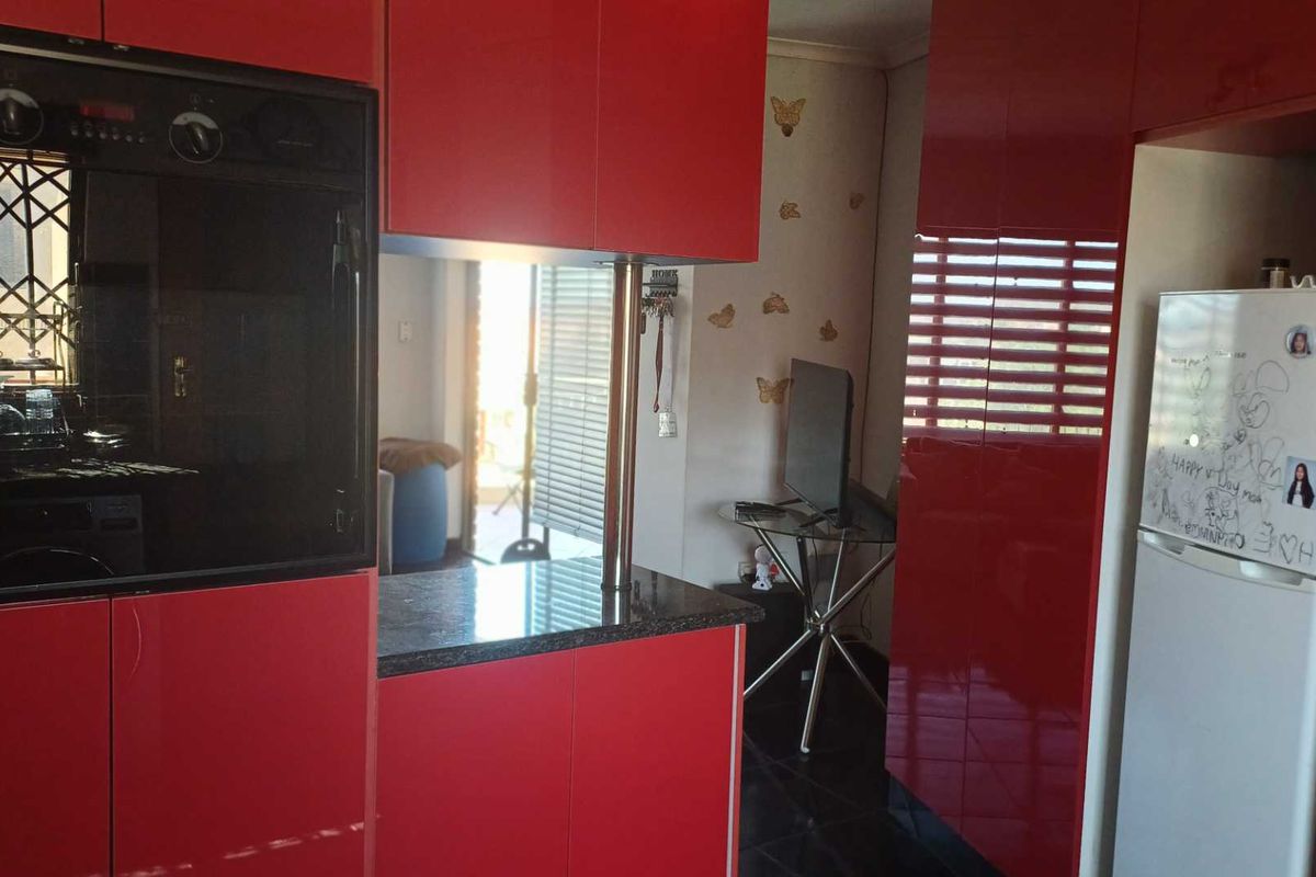 Kitchen area featuring high-gloss red cabinetry, a built-in oven, and a granite countertop with a breakfast bar support pillar.