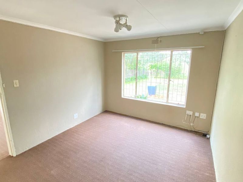 An empty bedroom featuring carpeted flooring, security bars on the window, and neutral wall tones, offering a blank canvas for potential updates.