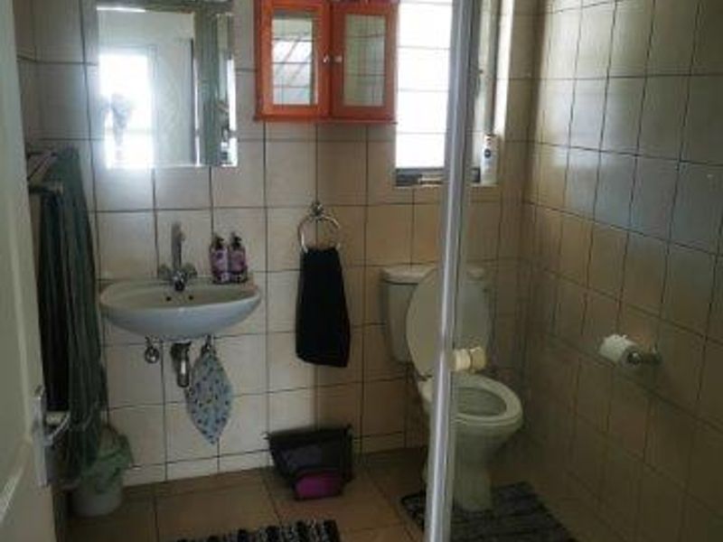 A functional bathroom featuring a wall-mounted basin, toilet, and a glass-enclosed shower with neutral ceramic tiling throughout.