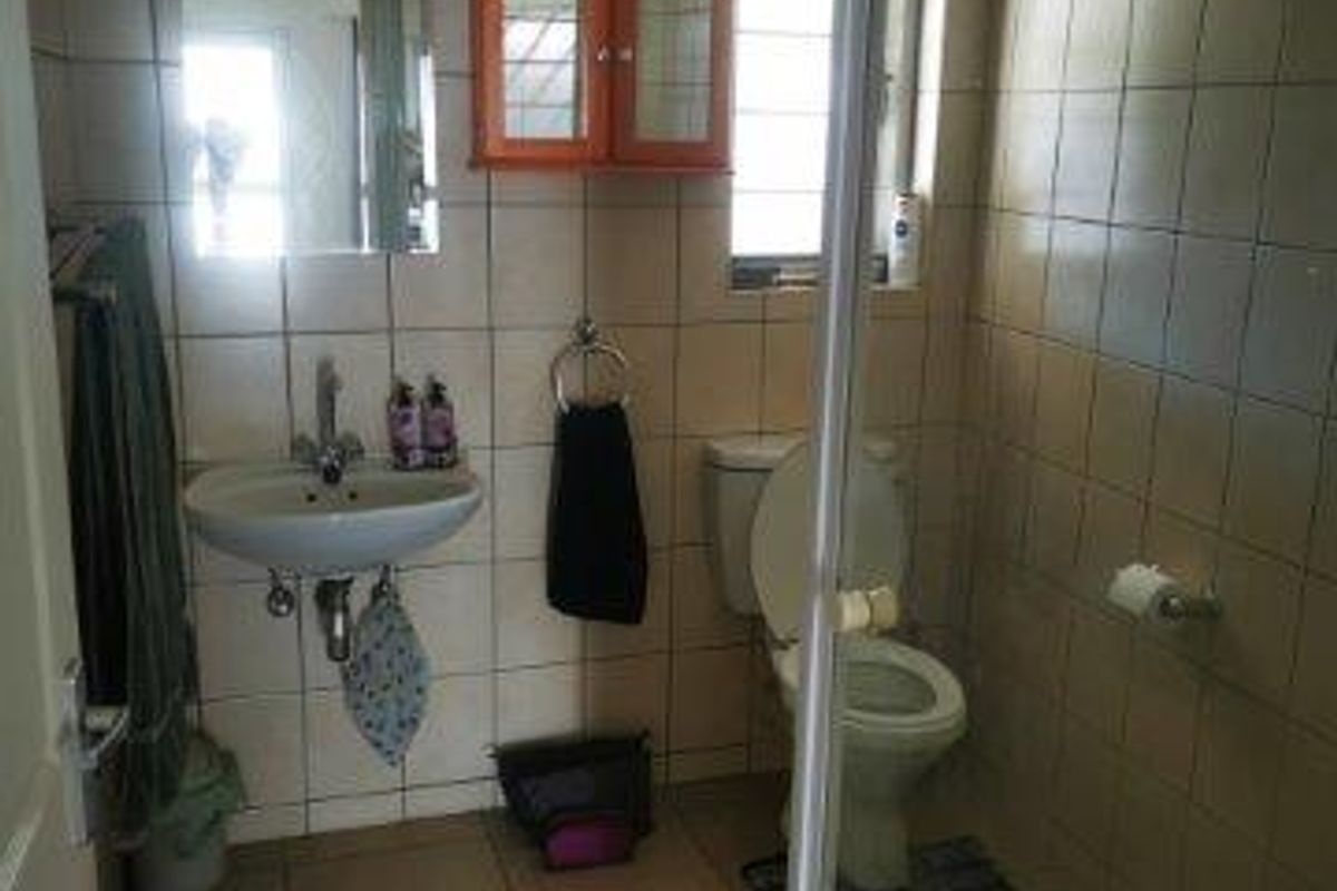 A functional bathroom featuring a wall-mounted basin, toilet, and a glass-enclosed shower with neutral ceramic tiling throughout.