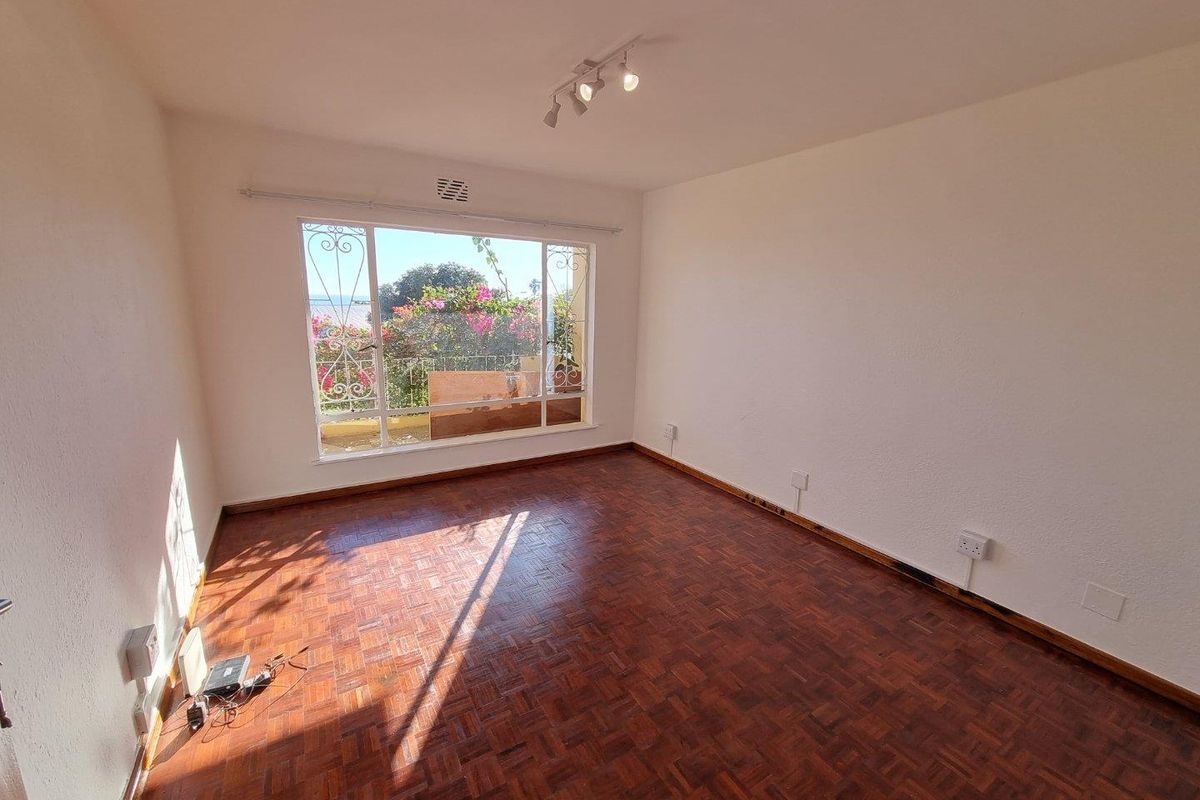 A bright, empty bedroom featuring original parquet flooring, large window with security bars, and ceiling-mounted spotlight fixtures.