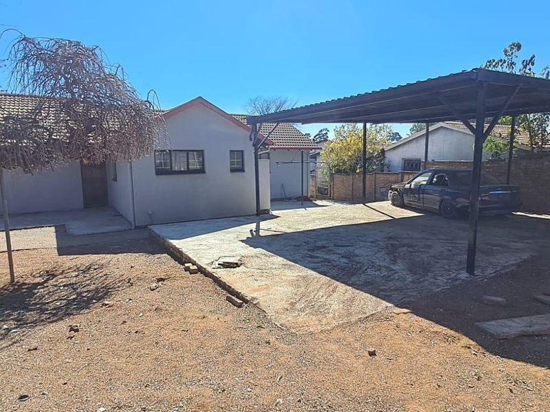 Rear exterior view of the property featuring a metal carport, concrete slab area, and brick boundary walling.