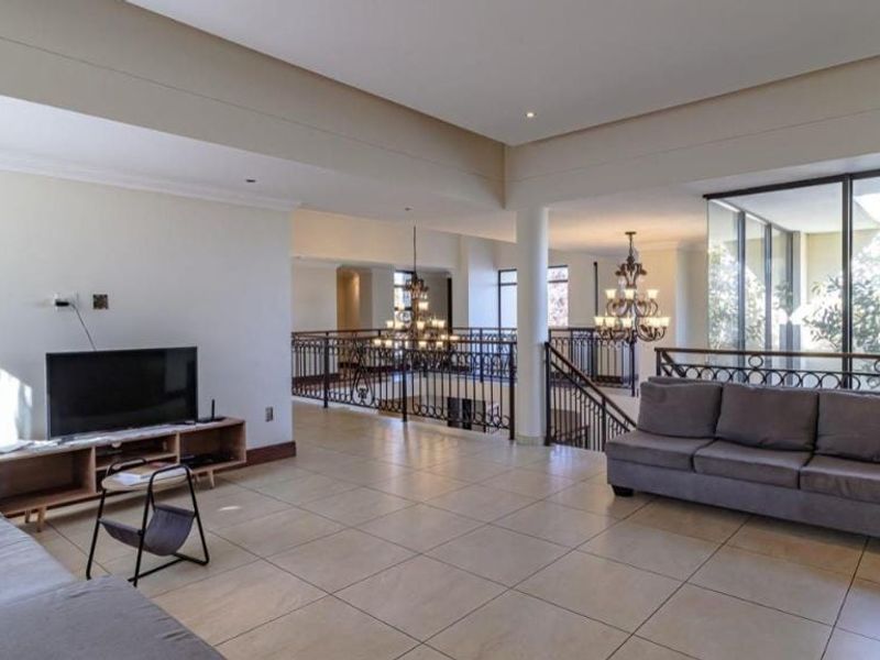 Spacious open-plan living area featuring large windows, tiled flooring, and a decorative wrought iron balustrade overlooking the lower level.