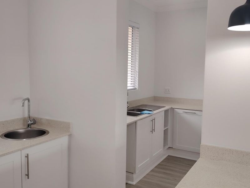 A clean, modern scullery area featuring white shaker cabinetry, stone countertops, and dual sink stations with neutral laminate flooring.