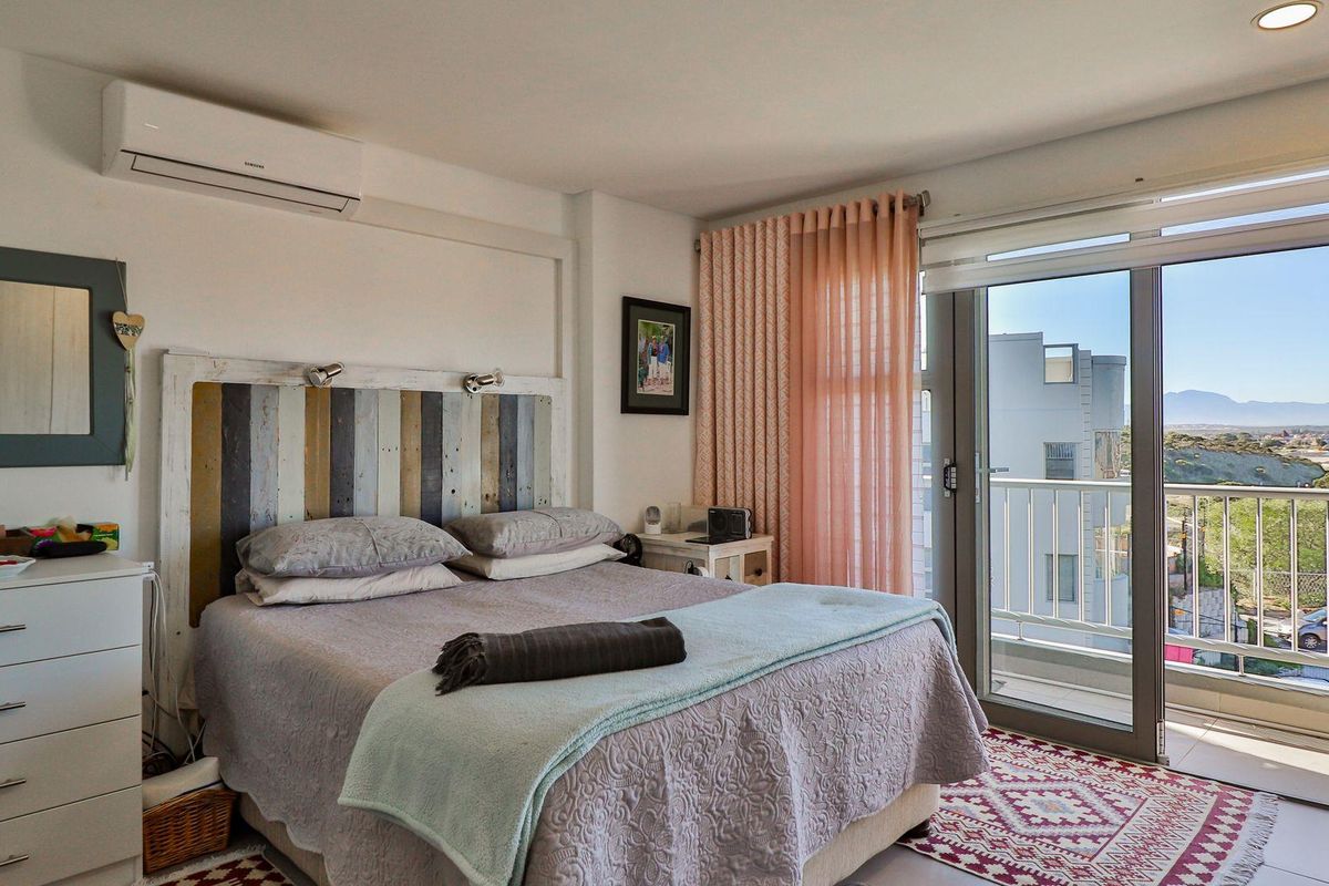 A bright bedroom featuring a wall-mounted air conditioning unit, tiled flooring, and large sliding glass doors leading to a private balcony with scenic views.