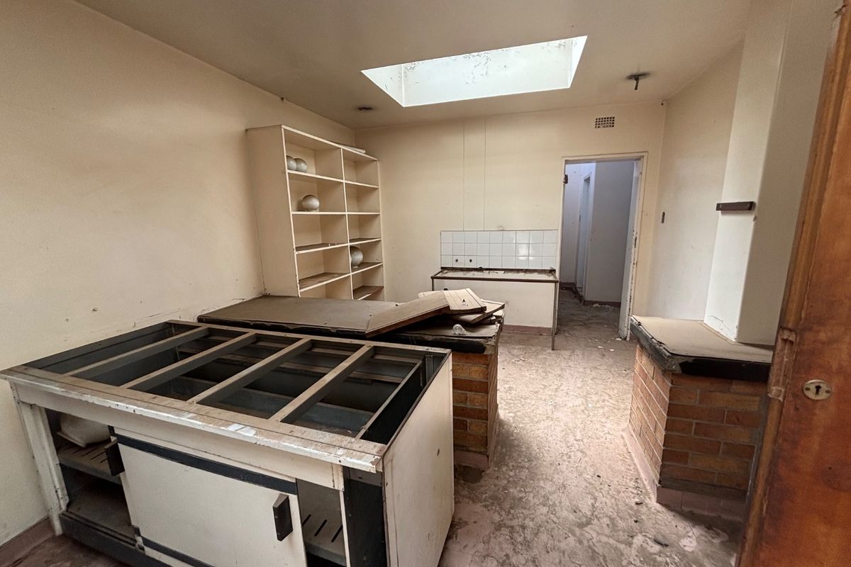 A dilapidated kitchen space featuring a skylight, brick-based cabinetry, and built-in shelving, requiring significant renovation and refurbishment.