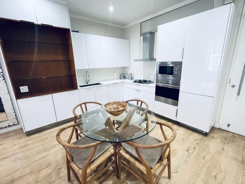Modern kitchen featuring high-gloss white cabinetry, integrated stainless steel appliances, gas hob, and durable laminate flooring.