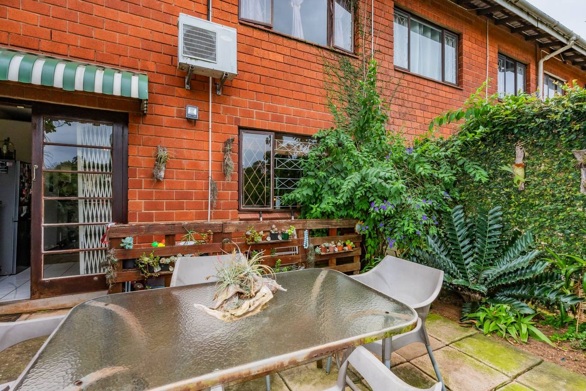 Rear exterior view of a townhouse featuring an exposed brick facade, paved patio area, and wall-mounted air conditioning unit.