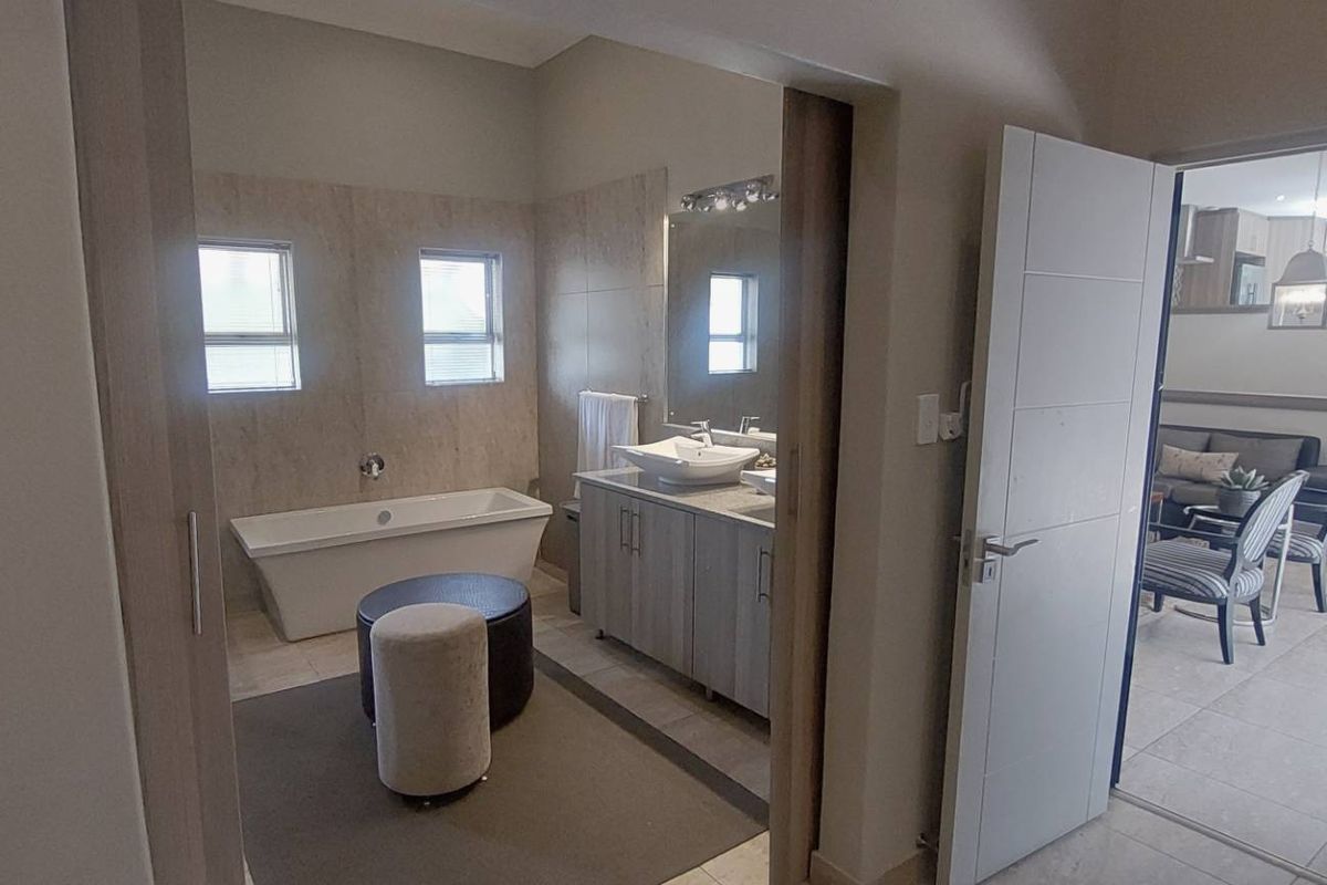 A modern bathroom featuring a freestanding bathtub, double vanity with storage, and neutral wall tiling, with an adjacent view into the living area.