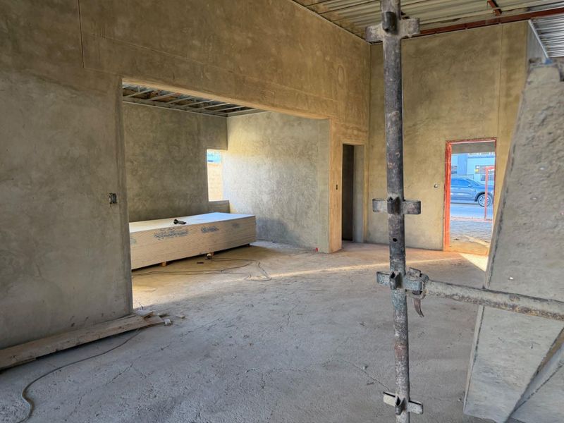 An interior view of an open-plan living space currently under construction, featuring exposed concrete walls and unfinished ceiling structures.