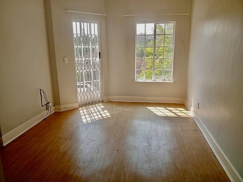 An empty bedroom featuring laminate flooring, a security gate, and a window with burglar bars, offering a blank canvas for personalization.