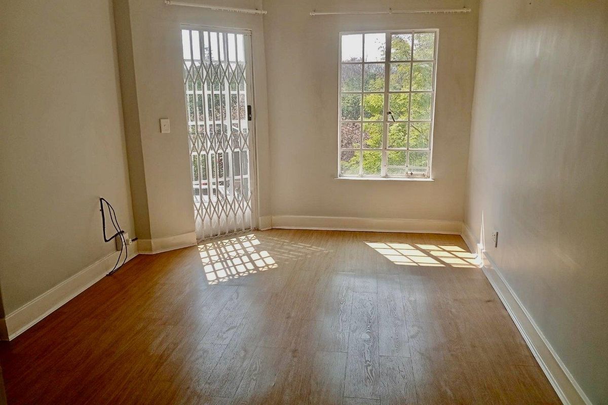 An empty bedroom featuring laminate flooring, a security gate, and a window with burglar bars, offering a blank canvas for personalization.