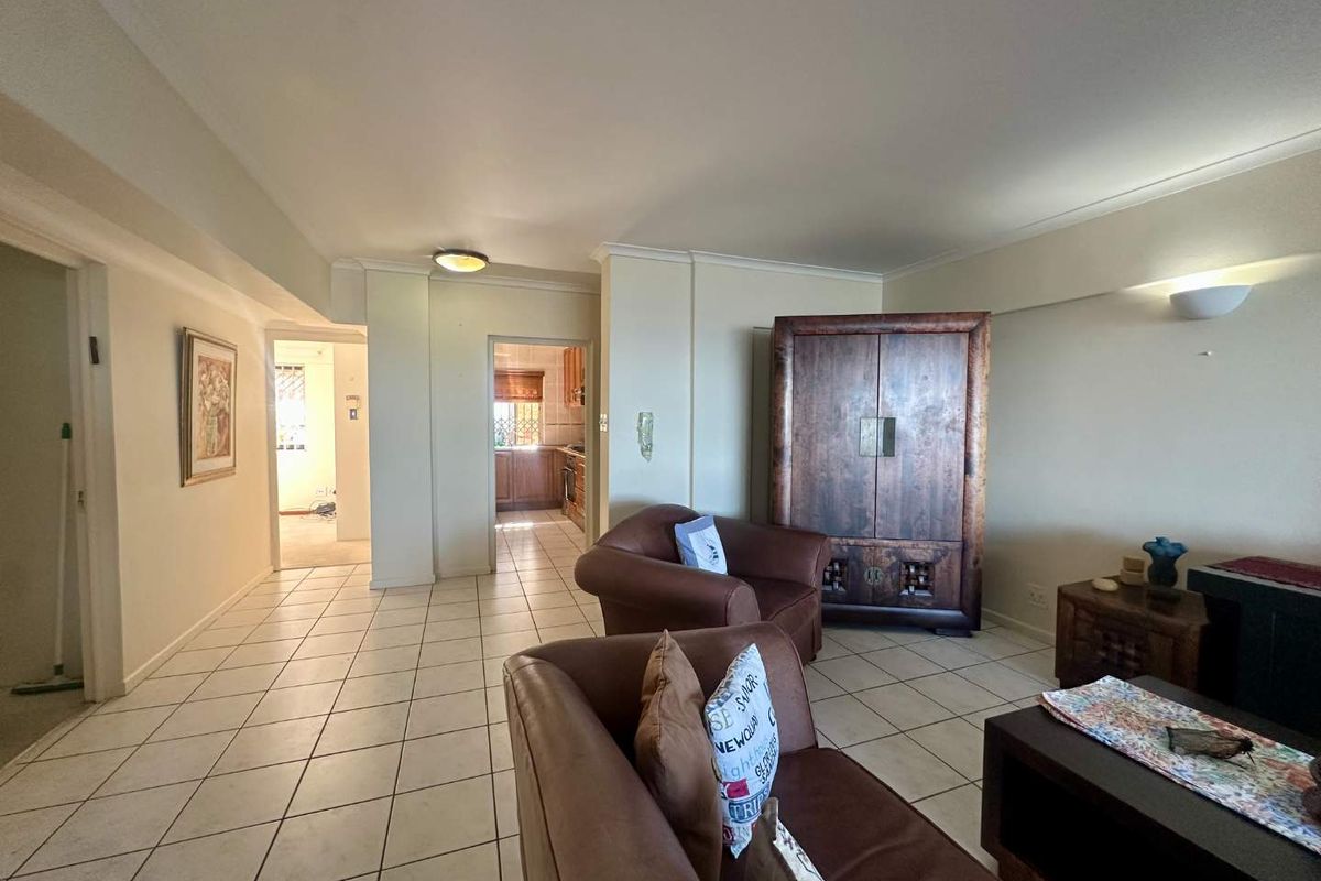 Spacious living area featuring neutral ceramic floor tiles and coved ceilings, with an open flow leading to the kitchen and hallway.