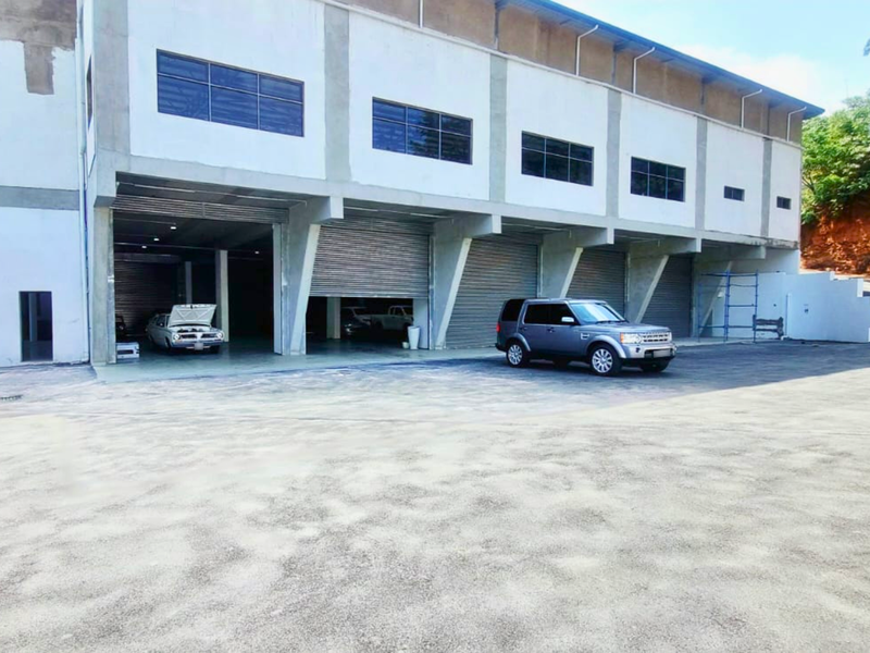 Industrial warehouse facility featuring multiple roller shutter doors, concrete construction, and a large paved yard area suitable for commercial or logistics operations.