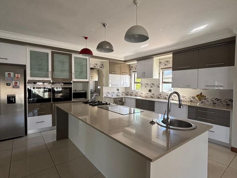 Modern kitchen featuring a large central island with stone countertops, built-in appliances, ample cabinetry, and tiled flooring.
