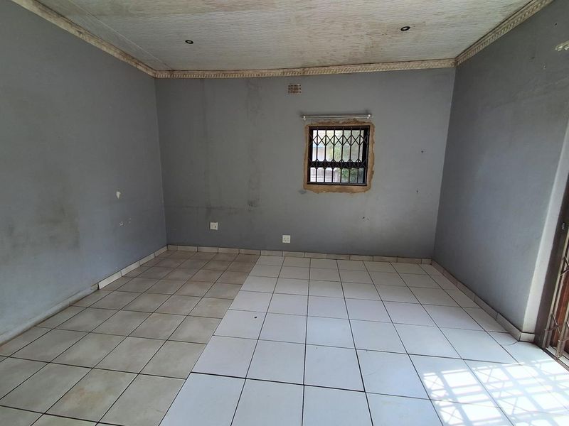 An empty living room featuring ceramic tiled flooring, security window bars, and recessed lighting, requiring cosmetic updates to the walls and ceiling.