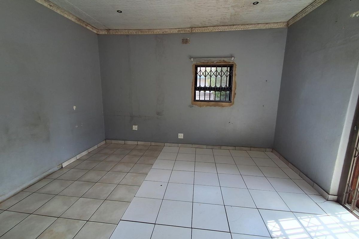 An empty living room featuring ceramic tiled flooring, security window bars, and recessed lighting, requiring cosmetic updates to the walls and ceiling.